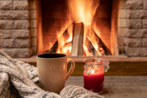 Big mug with hot tea, and a candle , wool scarf, near cozy fireplace, hygge, home sweet home.